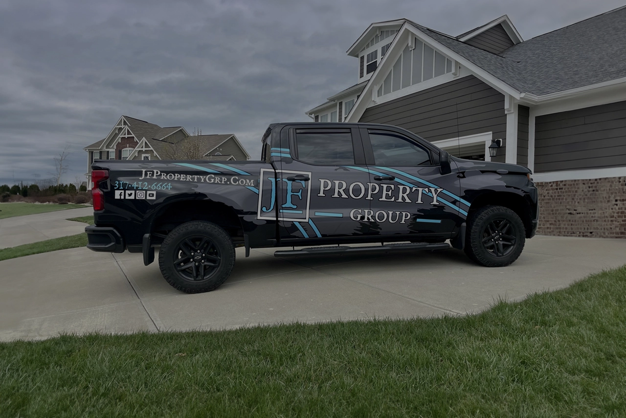 A shadowed view of the JF Property Group truck, with its recognizable decals displayed on the side, parked neatly in a driveway. The dim lighting adds a dramatic effect to the truck, highlighting its branding amidst the quiet surroundings.